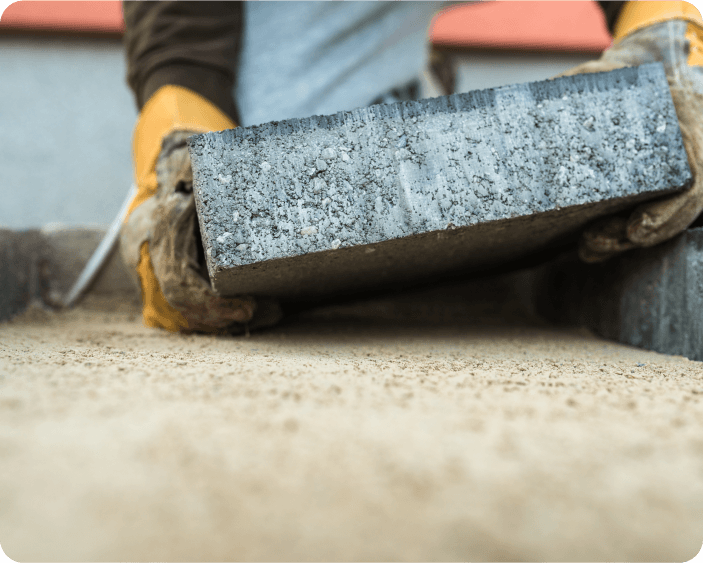 Worker laying a concrete paving stone on sand